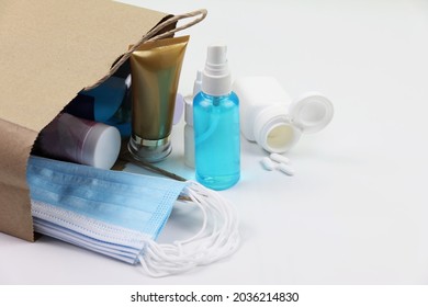 Alcohol In Spray Bottle With Medical Masks And Covid-19 Protective Gear In Brown Paper Bag On White Background.