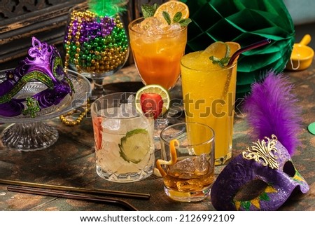 Alcoholic beverage cocktails, purple, green and gold Mardi Gras beads, masks decoration on dark rustic background, festive holiday concept