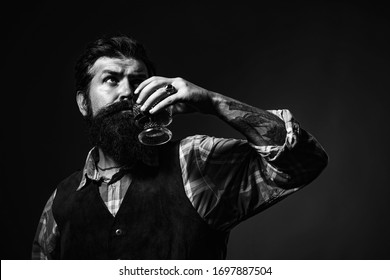 Alcoholic Beverage. Confident Bearded Man In Black Suit With Glass Of Whisky In Loft. Man Drinking Alcohol From Glass. Stylish Rich Man Holding A Glass Of Old Whisky