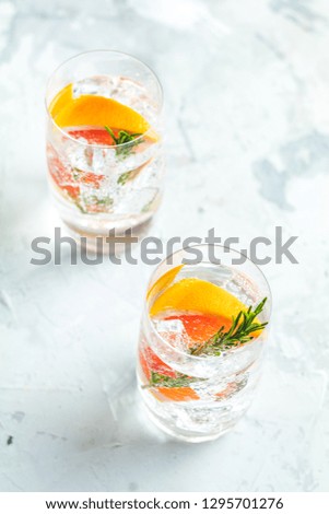 Alcoholic cocktail with grapefruit, soda, ice, gin and rosemary, light gray concrete table background, selective focus, shallow depth of the field.