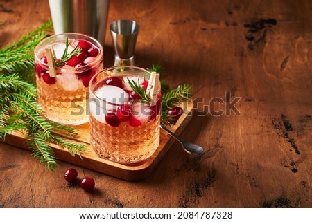 Alcoholic cocktail or non-alcoholic cocktail with vodka and cranberries with ice, shaker, jigger and bar spoon, fir branches and glowing garland for christmas on wooden background.