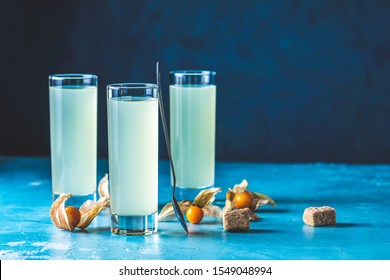 Alcoholic Cocktail With Ouzo Greek Anise Brandy Or Arabic Alcohol Drink Raki In Highball Glass, Decorated Physalis Peruviana And Brown Sugar On Blue Concrete Surface.