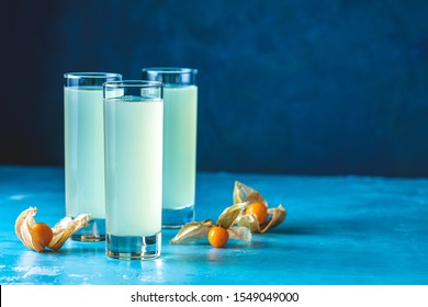 Alcoholic Cocktail With Ouzo Greek Anise Brandy Or Arabic Alcohol Drink Raki In Highball Glass, Decorated Physalis Peruviana And Brown Sugar On Blue Concrete Surface.