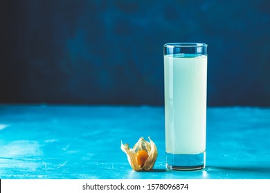 Alcoholic Cocktail With Ouzo Greek Anise Brandy Or Arabic Alcohol Drink Raki In Highball Glass, Decorated Physalis Peruviana And Brown Sugar On Blue Concrete Surface.