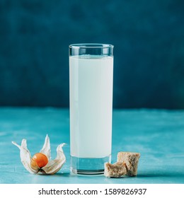 Alcoholic Cocktail With Ouzo Greek Anise Brandy Or Arabic Alcohol Drink Raki In Highball Glass, Decorated Physalis Peruviana And Brown Sugar On Blue Concrete Surface.