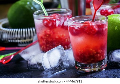 Alcoholic cocktail raspberry ambitions, with vodka, cranberry juice, soda, lime, berries and ice, bar tools, black background, selective focus