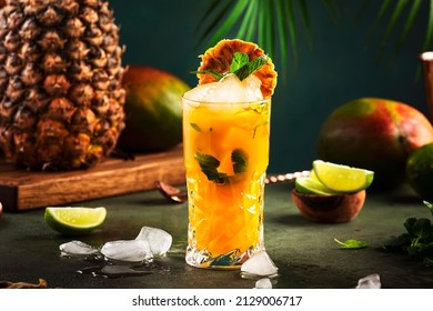 Alcoholic Cocktail With Vodka, Pineapple Juice, Mango, Liquor, Ice. Long Drink Or Summer Cold Mocktail. Tropical Dark Background With Palm Leaves And Exotic Fruits