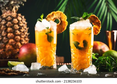 Alcoholic Cocktail With Vodka, Pineapple Juice, Mango, Liquor, Ice. Long Drink Or Summer Cold Mocktail. Tropical Dark Background With Palm Leaves And Exotic Fruits