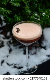 Alcoholic Coffee Cocktail In The Snow On A Background Of Greenery
