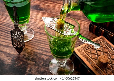 Alcoholic drink, creative stimulant and bohemian lifestyle concept theme with a vintage glass bottle pouring absinthe over a sugar cube in a stainless steel spoon next to books on a wooden table