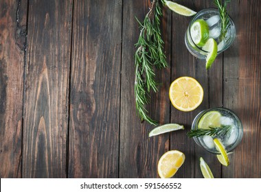 Alcoholic drink gin tonic cocktail with lemon, rosemary and ice on rustic wooden table, copy space.