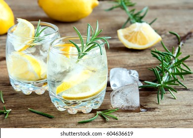 Alcoholic drink (gin tonic cocktail) with lemon, rosemary and ice on rustic wooden table, copy space
