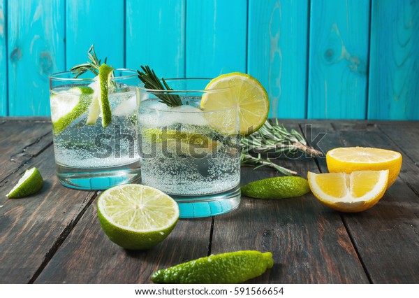 Alcoholic drink gin tonic\
cocktail with lemon, rosemary and ice on rustic wooden table, copy\
space