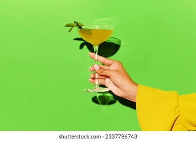 Alcoholic drink. Hand holding high glass with bronx cocktail over bright green background. Concept of alcohol, drinks, pop art, party and relax. Copy space for ad