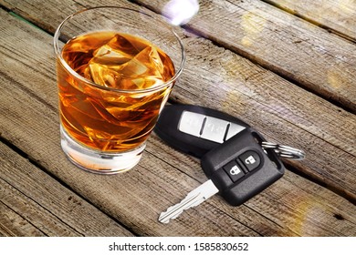 Alcoholic drink with ice in a glass and car keys on a wooden desk