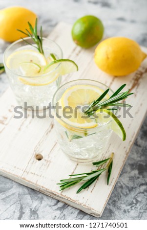 Alcoholic drink with lemon and rosemain in glasses on a light table