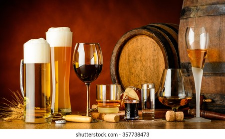 alcoholic drinks on wooden table in glasses, mugs and shots with barrel in background