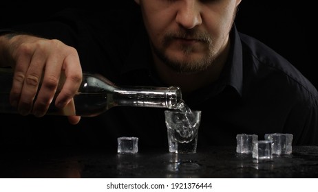 Alcoholic guy drinking cold transparent alcohol drink sake, tequila or rum. Man pouring up frozen vodka from bottle into shot glass with ice cubes on black background. Alcohol dependence addiction