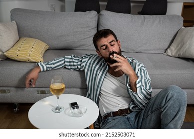 Alcoholic Man Holding A Cigarette With Alcohol Drink In The Glass On The Table And Smoking Cigarette. Addiction Concept. Male Addict Drinking Alcohol And Smoke Alone At Home