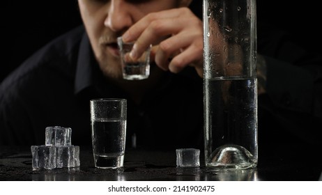 Alcoholic man pouring up frozen vodka from bottle into shot glass with ice cubes on black background. Guy drinking cold transparent alcohol drink sake, tequila or rum. Alcohol dependence addiction