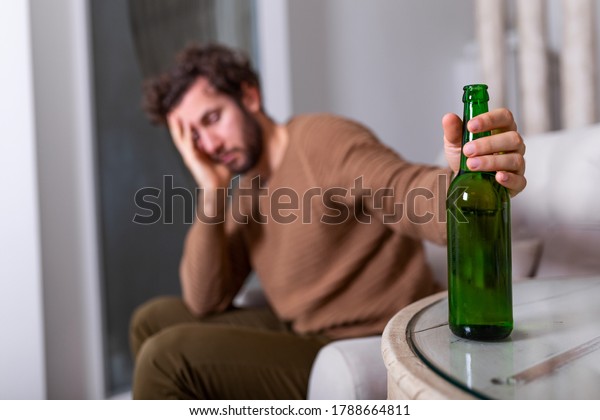 Alcoholic man\
reaching for bottle of beer, Man drinking home alone. alcoholism,\
alcohol addiction and people concept - male alcoholic with bottle\
of beer drinking at home\
alone