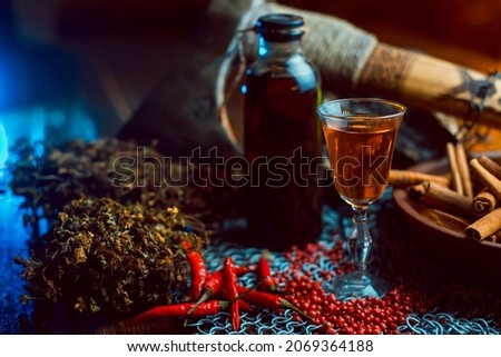 Alcoholic pepper tincture with spices. On chain mail. Ax and dried herbs with cinnamon on a background