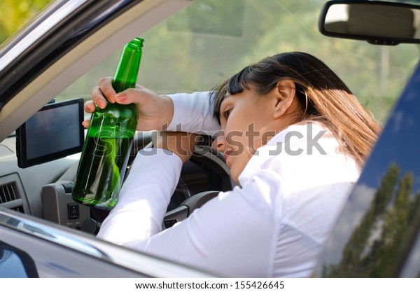 Alcoholic woman driver passed out in the car with\
her head resting on her arm on the steering wheel and her bottle of\
booze clasped in her\
hand
