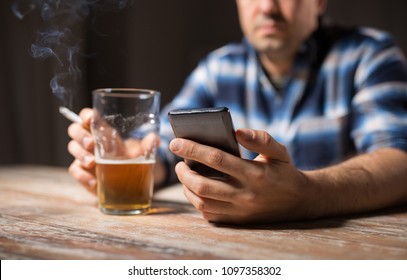 Alcoholism, Alcohol Addiction And People Concept - Male Alcoholic With Smartphone Drinking Beer And Smoking Cigarette At Night