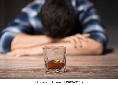 alcoholism, alcohol addiction and people concept - male alcoholic with glass of whiskey lying or sleeping on table at night
