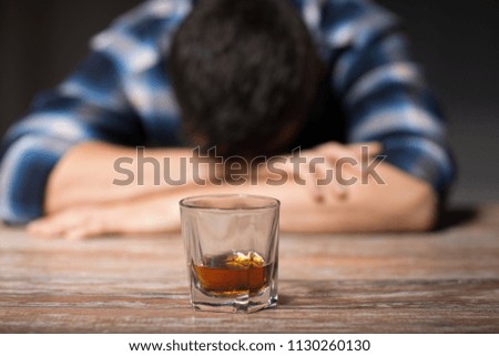 alcoholism, alcohol addiction and people concept - male alcoholic with glass of whiskey lying or sleeping on table at night