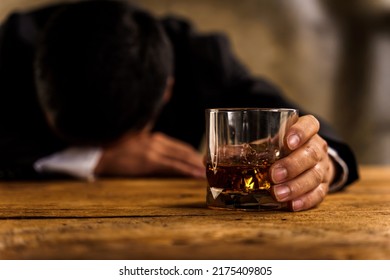 Alcoholism, Depressed Asian Young Man Sleep On Table While Drinking Alcoholic Beverage, Holding Glass Of Whiskey Alone At Night. Treatment Of Alcohol Addiction, Suffer Abuse Problem Alcoholism Concept