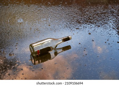 Alcoholism Problem Concept. Empty Bottle Of Liquor On A Wet Floor After Rain At Sunset