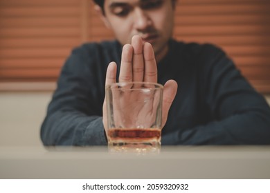 Alcoholism, sad depressed asian young man refuse, push alcoholic beverage glass, drink whiskey, sitting alone at night. Treatment of alcohol addiction, having suffer abuse problem alcoholism concept.