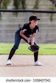 Alert Female Softball Infielder Crouched Down Into Ready Position And Prepared For The Ball.