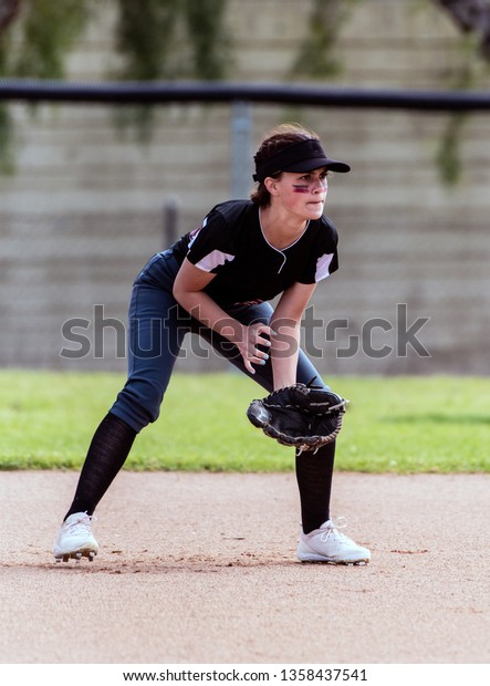 Alert female softball infielder\
crouched down into ready position and prepared for the\
ball.