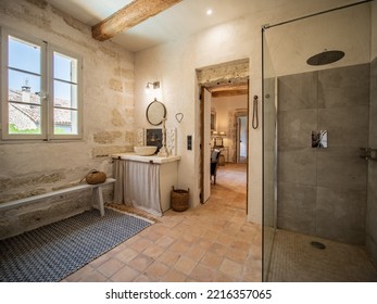 Ales, France - June 16th 2022 : Luxurious And Rustic Bathroom, Stone Floor And Wall, Other White Walls, Large Open Shower, White Window On The Left, Striped Carpet, Visible Wooden Beam On The Ceiling