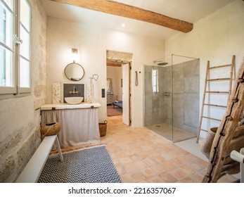 Ales, France - June 16th 2022 : Luxurious And Rustic Bathroom, Stone Floor And Wall, Other White Walls, Large Open Shower, White Window On The Left, Striped Carpet, Visible Wooden Beam On The Ceiling