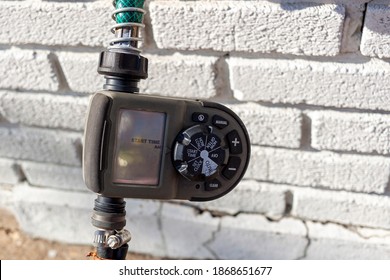 Alexandria, VA, USA 11-28-2020: Close Up Digital Hose Timer Attached To Garden Hose Coming Out Of A Brick House. Inlet And Outlet Hoses Are Screwed In And The Electronic Timer  Regulates Water Flow.