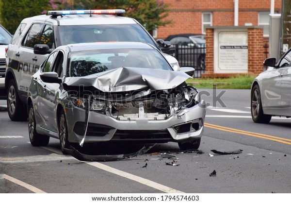 Alexandria,VA/USA-8/6/20: Car accident\
front view. Single car smashed and destroyed front with police car\
in background. Daytime street\
intersection.
