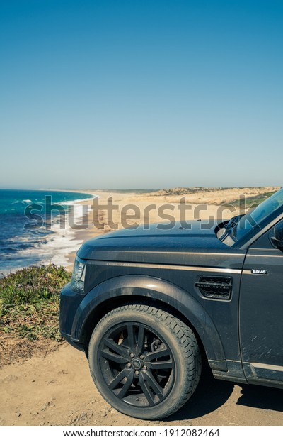 Algarve, Portugal - August 2020: Lifestyle\
photo of a black Land Rover Discovery 4 driving along scenic\
Portuguese coastline.