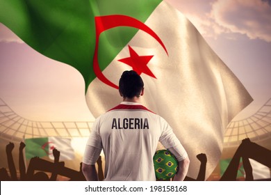 Algeria Football Player Holding Ball Against Large Football Stadium Under Bright Blue Sky