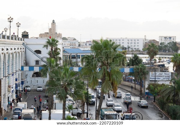 Algiers city, Algeria - September 16, 2022:\
fishery Port of Algiers, high angle view from Boulevard Che\
Guevara, people, cars and palm trees in foreground, the Admiralty\
lighthouse in\
background.