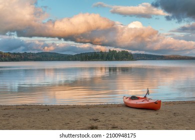 ALGONQUIN PARK, CANADA - Nov 12, 2021: A scene of a lake with beautiful sunset sky and forest reflection with a canoe on a sandy shore in Canada
