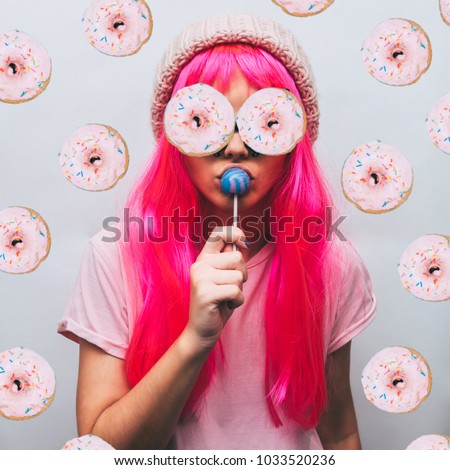 alien girl with donuts for eyes and the beanie hat is sucking candy