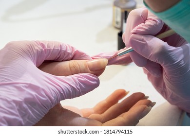 Alignment With A Thin Brush Applying A Base UV Varnish To The Nail. The Master In Pink Gloves Holds The Client's Hand.