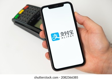 Alipay payment for online shopping with wireless POS payment terminal on the background. Man holding a mobile phone with app for payment. November 2021, San Francisco, USA