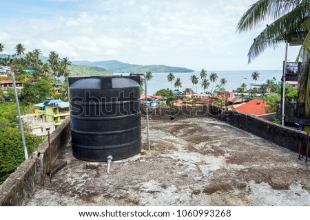 All city roofs are occupied by black water storage tanks and different satellites. Water tank on the roof in Asia. Water heating tank against sea and the city. Asian water supply and heating system