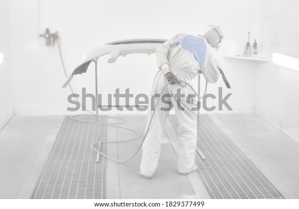 All in a haze of paint. Worker painting parts of
the car in special painting chamber, wearing costume and protective
gear. Car service station.