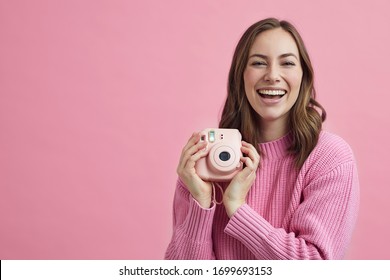 All pink concept with attractive girl holding a polaroid camera smiling to the viewer
