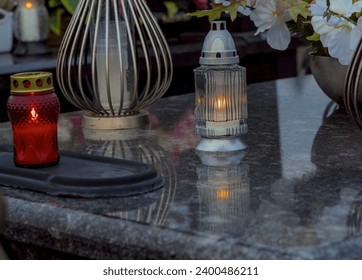 All Saints - burning candles and beautiful flowers on the tombstone after dark.On the shiny granite slab of the tombstone there are burning candles and standing flowers to commemorate the deceased .